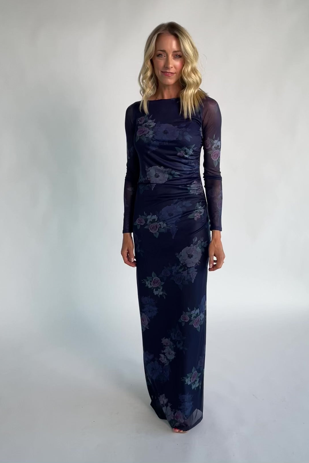 Model wearing a deep plum floral maxi dress with a fitted bodycon silhouette, sheer long sleeves, and a round neckline.