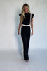 Model wearing the Lumina Ruffle Jumpsuit in Black + Ivory featuring a sleeveless ruffle-trim bodice, defined waist, and flowing wide-leg pants.