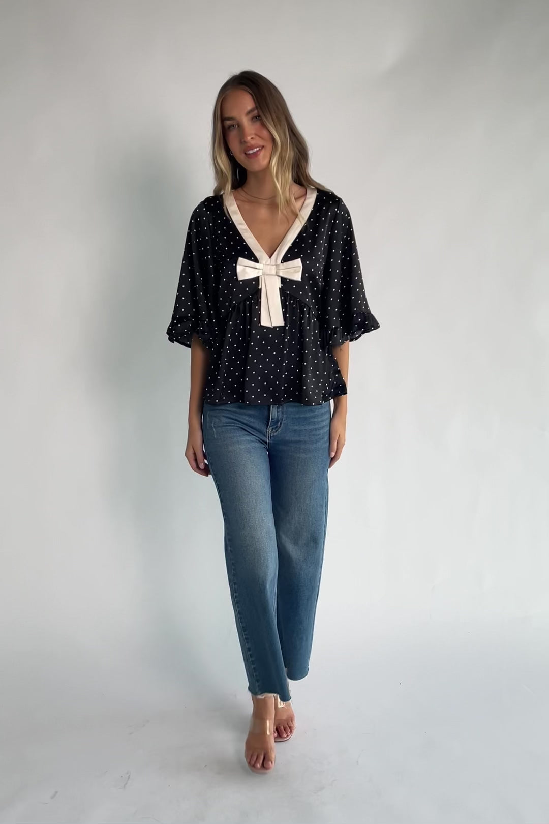 Black satin polka dot peplum top with an ivory contrast collar, decorative bow, V-neckline, and elbow-length ruffle sleeves.