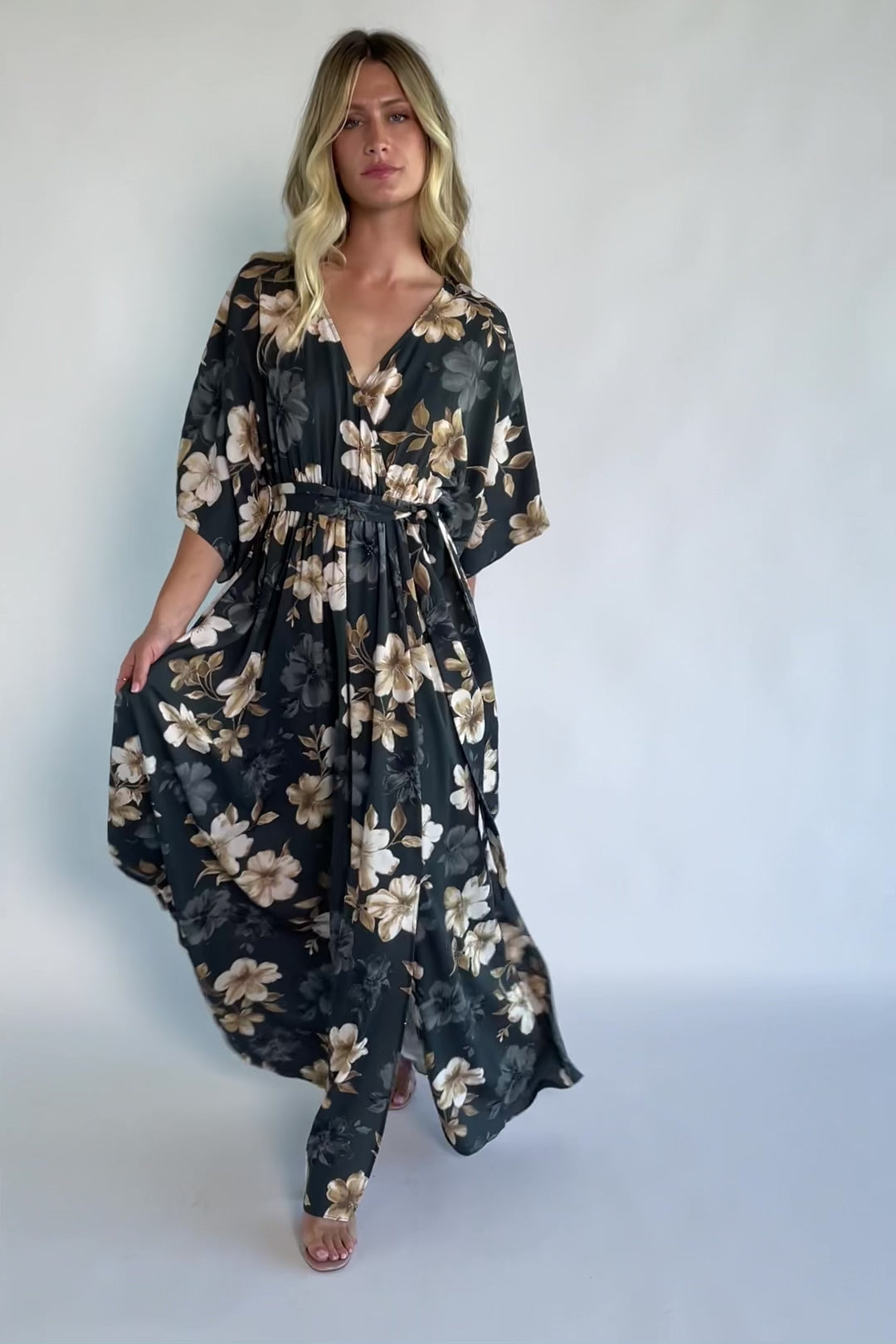 Model wearing a dark jade floral maxi dress with a surplice V-neckline, kimono sleeves, and an elastic waist with a removable sash tie.