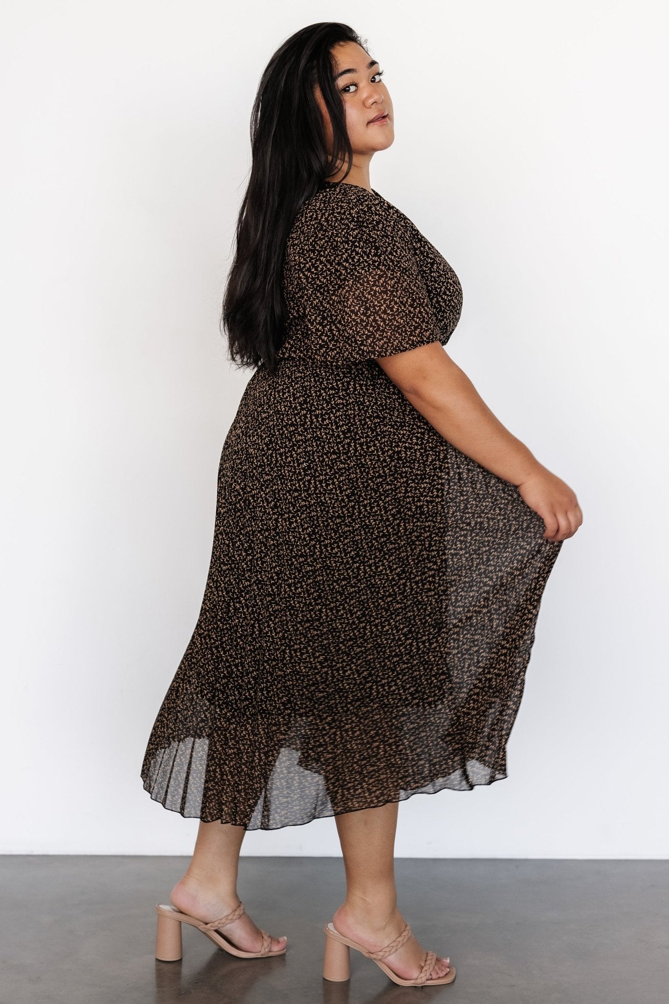 Styled look of the Prim Pleated Midi Dress worn with minimal accessories to showcase pleated movement and modest midi length in black print.