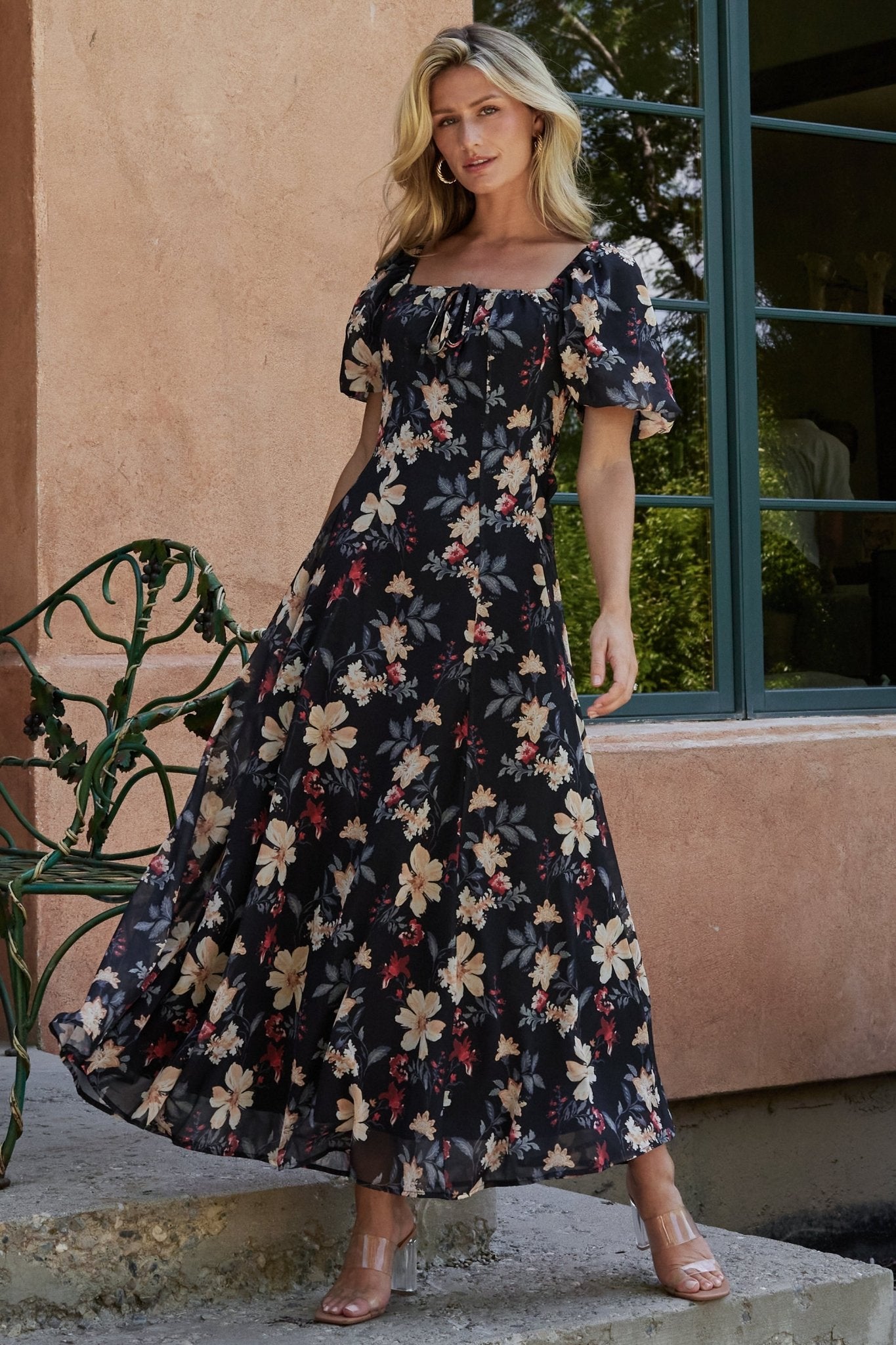 Front view of black floral maxi dress showing square neckline, tie detail, and corset-like front seams in soft floral print.