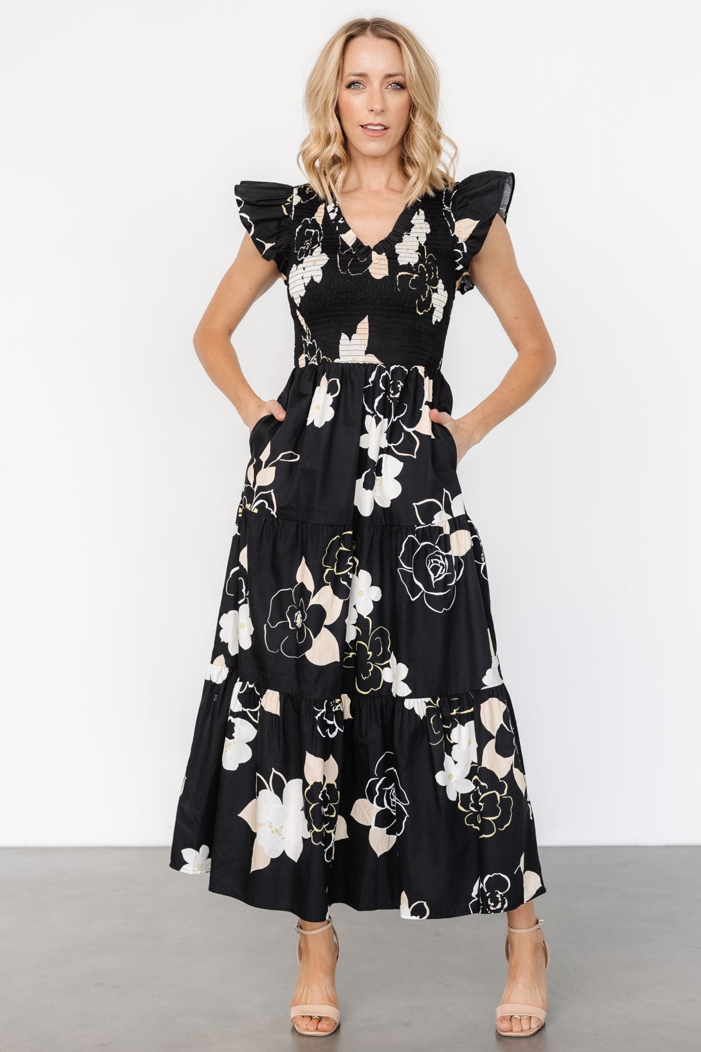 Front view of Ranchero smocked maxi dress in black floral print showing ruffled V-neck, smocked bodice, short ruffle sleeves and flowing tiered skirt.