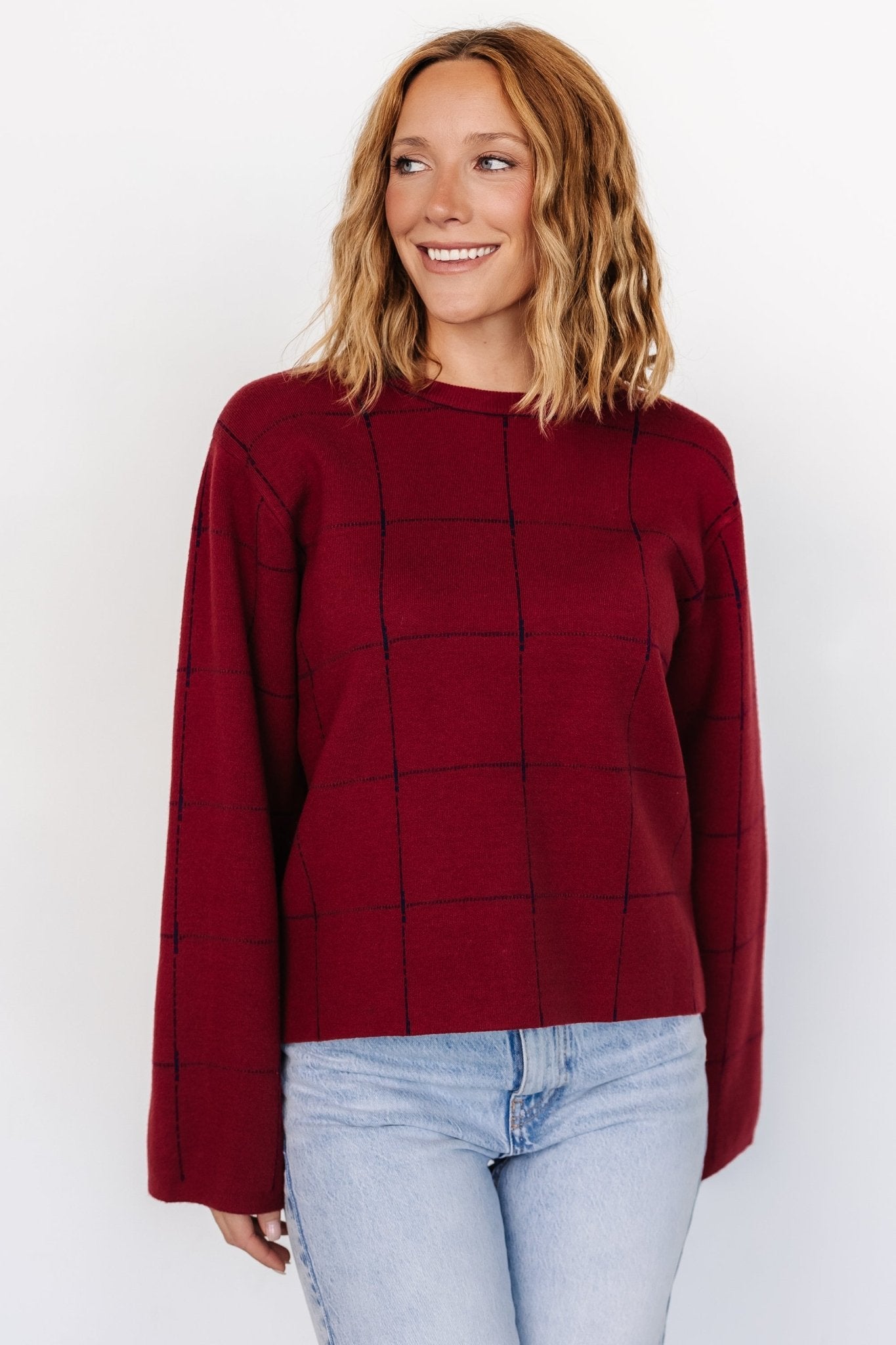 Front view of Remington Sweater in red with navy windowpane pattern on model; relaxed boxy fit, round neckline, and wide uncuffed sleeves for layering.