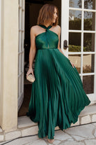 Front view of emerald pleated halter maxi dress on model, showing high criss-cross neckline, keyhole bust, lined bodice, and flowing pleated skirt.