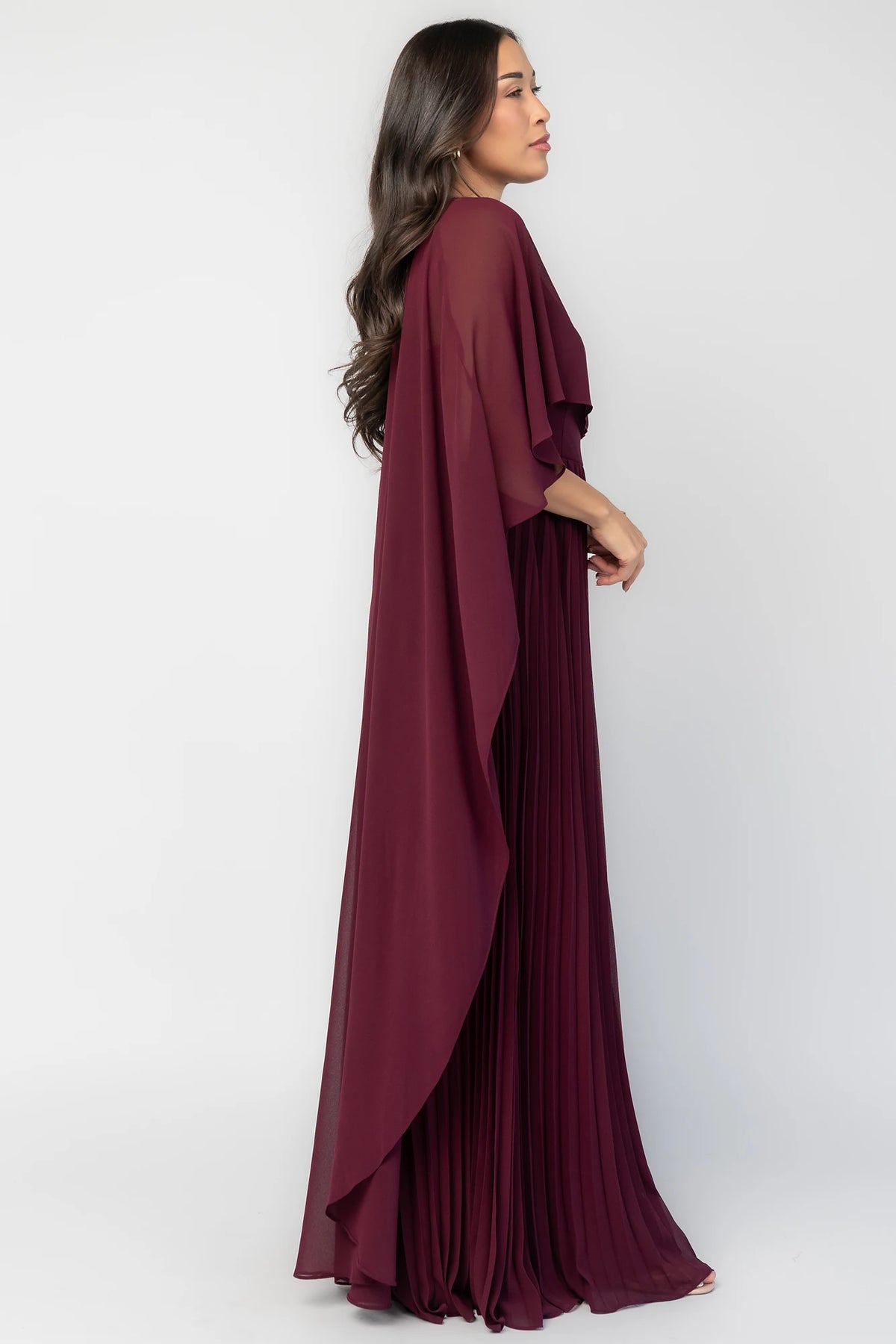 Serafina Strapless Gown in Burgundy with strapless neckline, removable sheer cape overlay, defined waist, and pleated skirt.