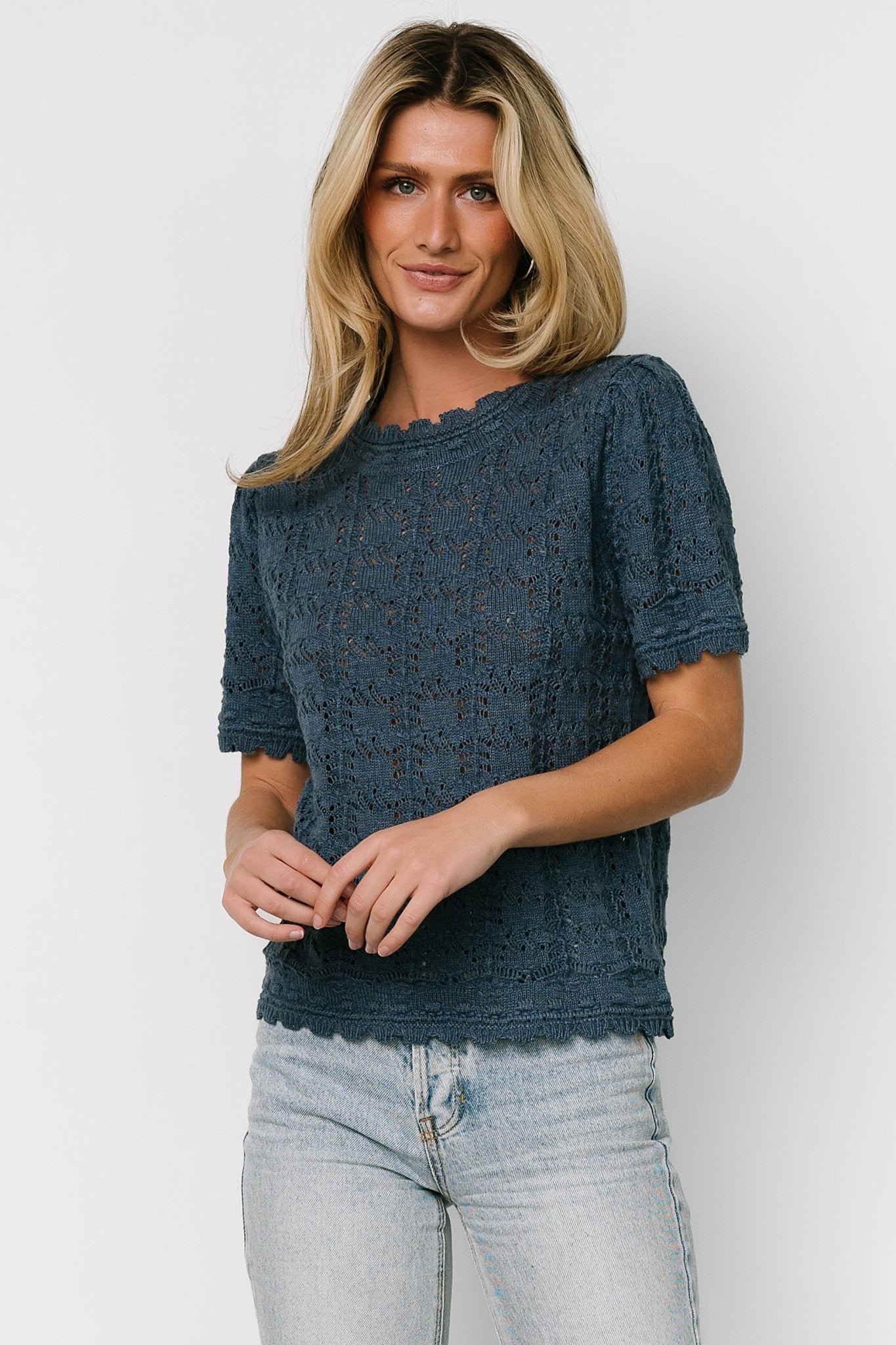 Close-up of scalloped collar and short sleeve of the Serenity crochet knit sweater top, highlighting delicate open-knit holes and stitch detail.