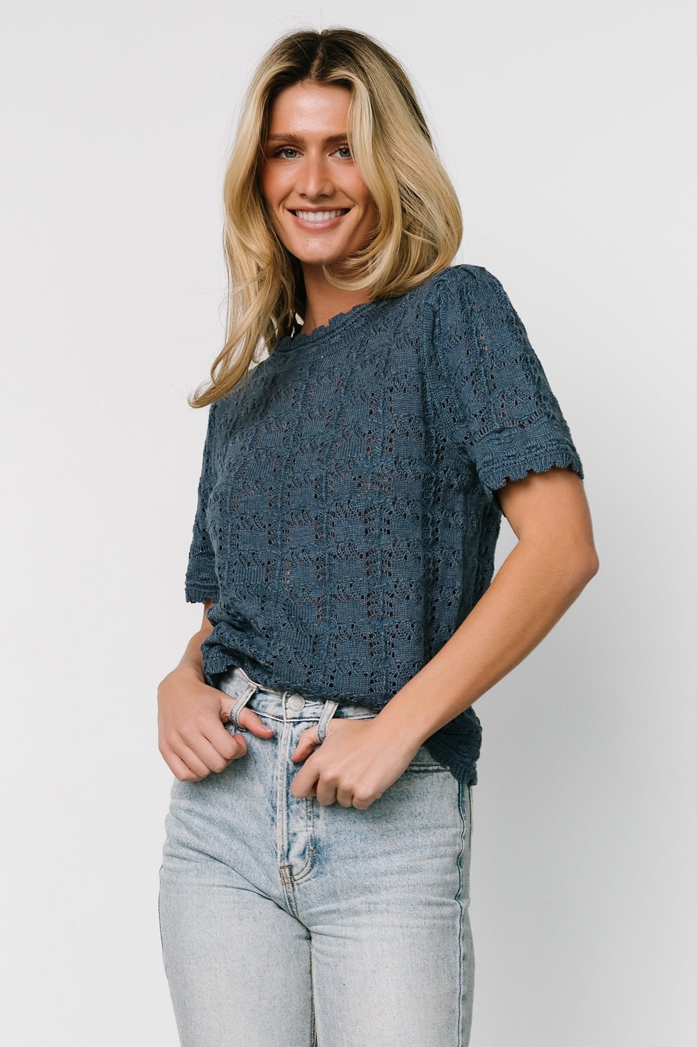 Front view of Serenity crochet knit sweater top in slate blue showing high neckline, short sleeves, scalloped collar, and open knit texture.