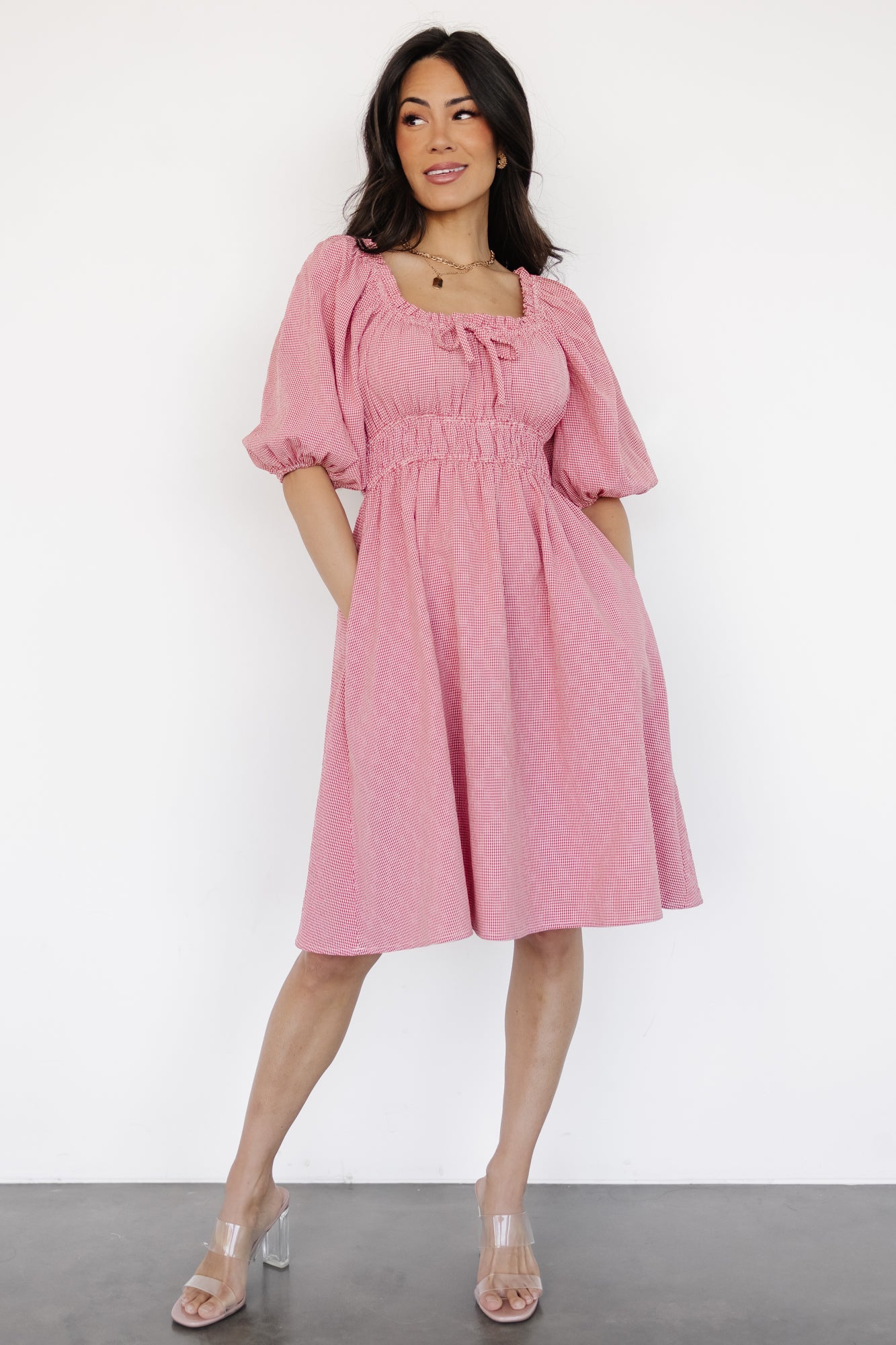 Front-facing photo of the Shawna short dress in red-and-off-white gingham, showing the elastic square neckline, decorative bust tie, and mini silhouette.