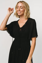 Three-quarter view of the black rayon midi dress on model, showing the flowing skirt, subtle gathered shoulder yoke and relaxed silhouette.