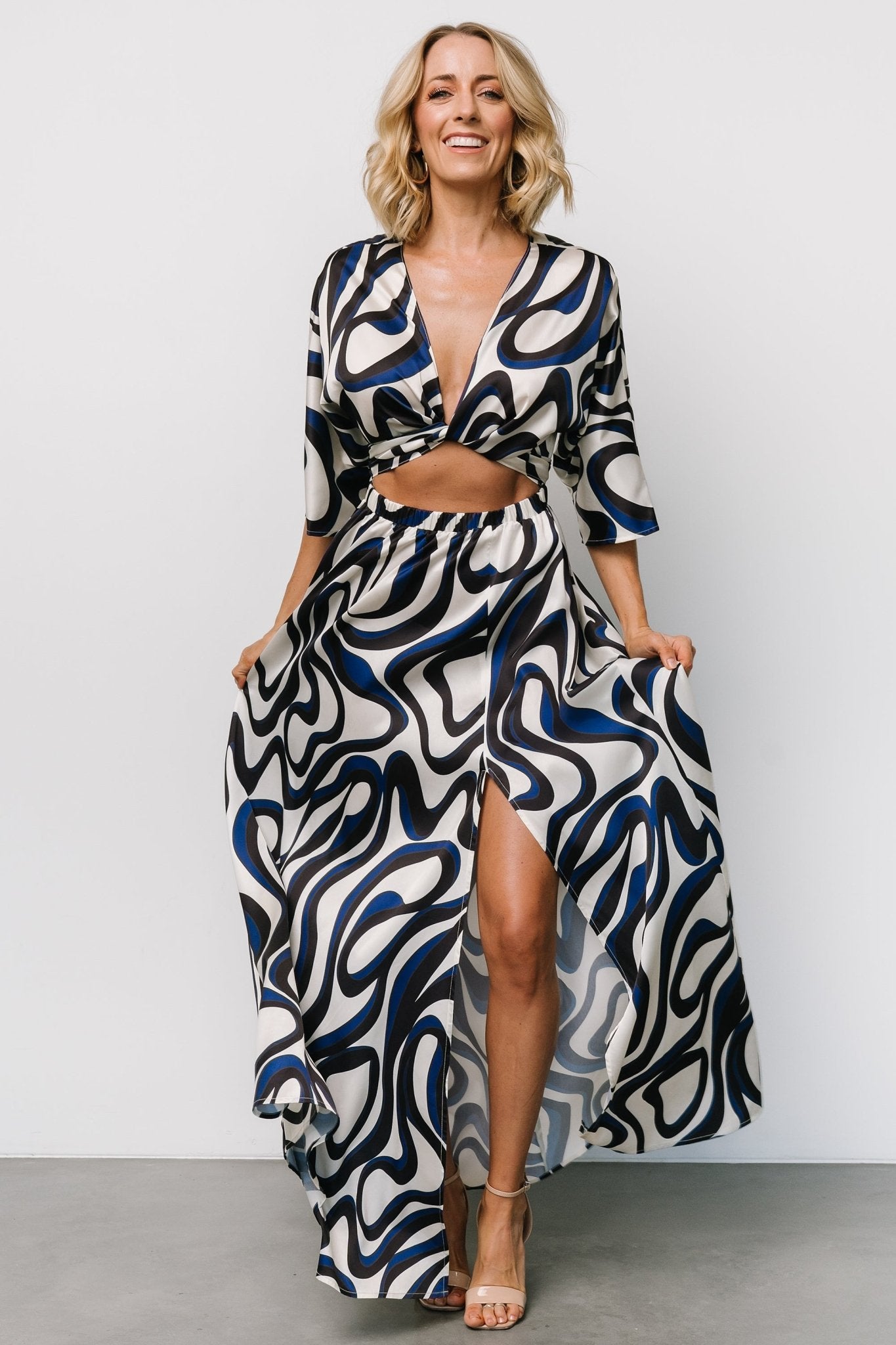 Three-quarter side view showing kimono-style sleeves, cut-out front bodice detail, elasticated waist and left leg slit on a flowing satin skirt.