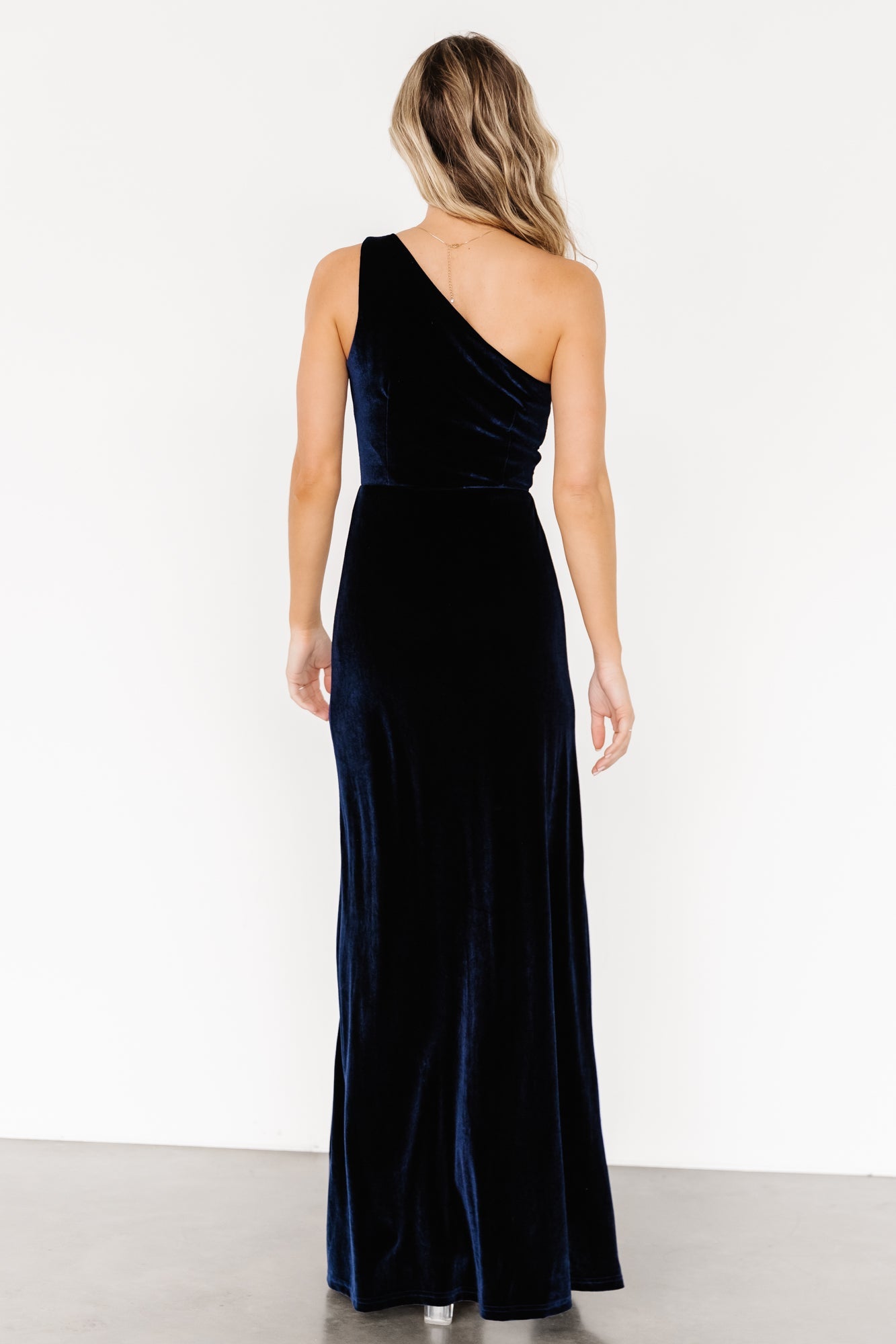 Angle view of Tatiana navy velvet dress on model with emphasis on slit, skirt movement, and overall evening-ready styling.
