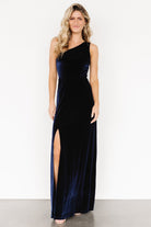 Full-length shot of Tatiana navy velvet maxi dress on model highlighting drape, floor-length hem, and elegant one-shoulder silhouette.
