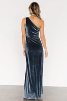 Model wearing Tatiana velvet one-shoulder maxi in slate blue, fitted through the bodice with a slight flare at the hem.