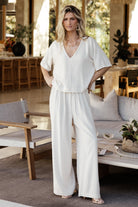 Model front view: natural linen-blend two-piece with V-neck short-sleeve top, center fabric detail, side split hem, and wide-leg pants.