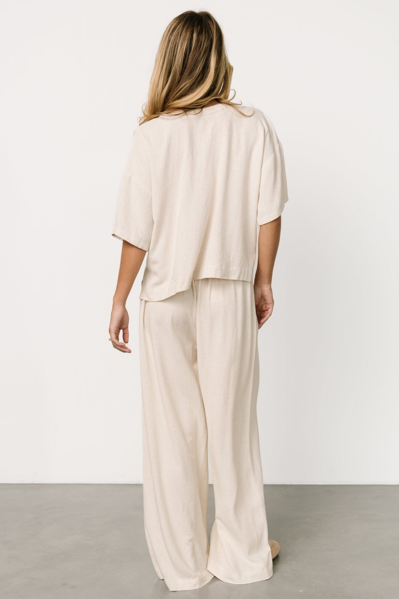 Back view of the natural two-piece set showing the relaxed silhouette and raw hem finish on the wide-leg pants.