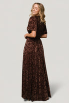 Side view of Veronica Velvet Maxi Dress in espresso on model, showing smocked stretch waist and the flowy short sleeves in motion.