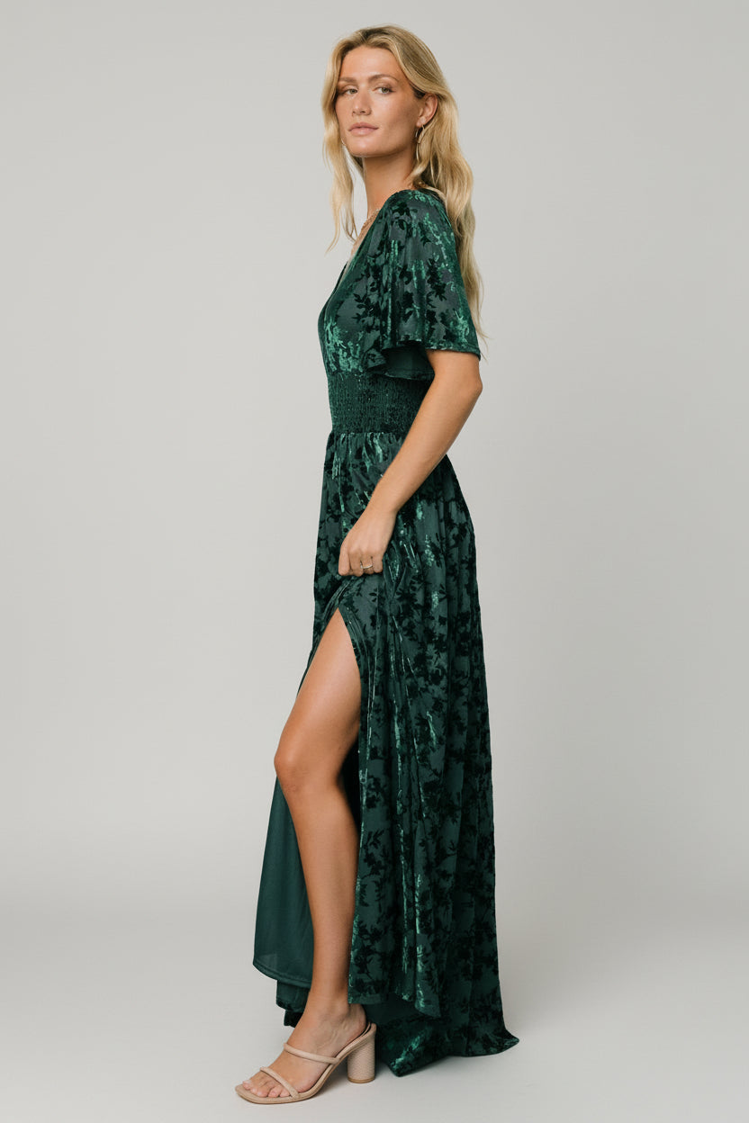 Close-up of embossed velvet fabric texture and smocked waist seam on the green maxi dress, showing fabric sheen and detail.