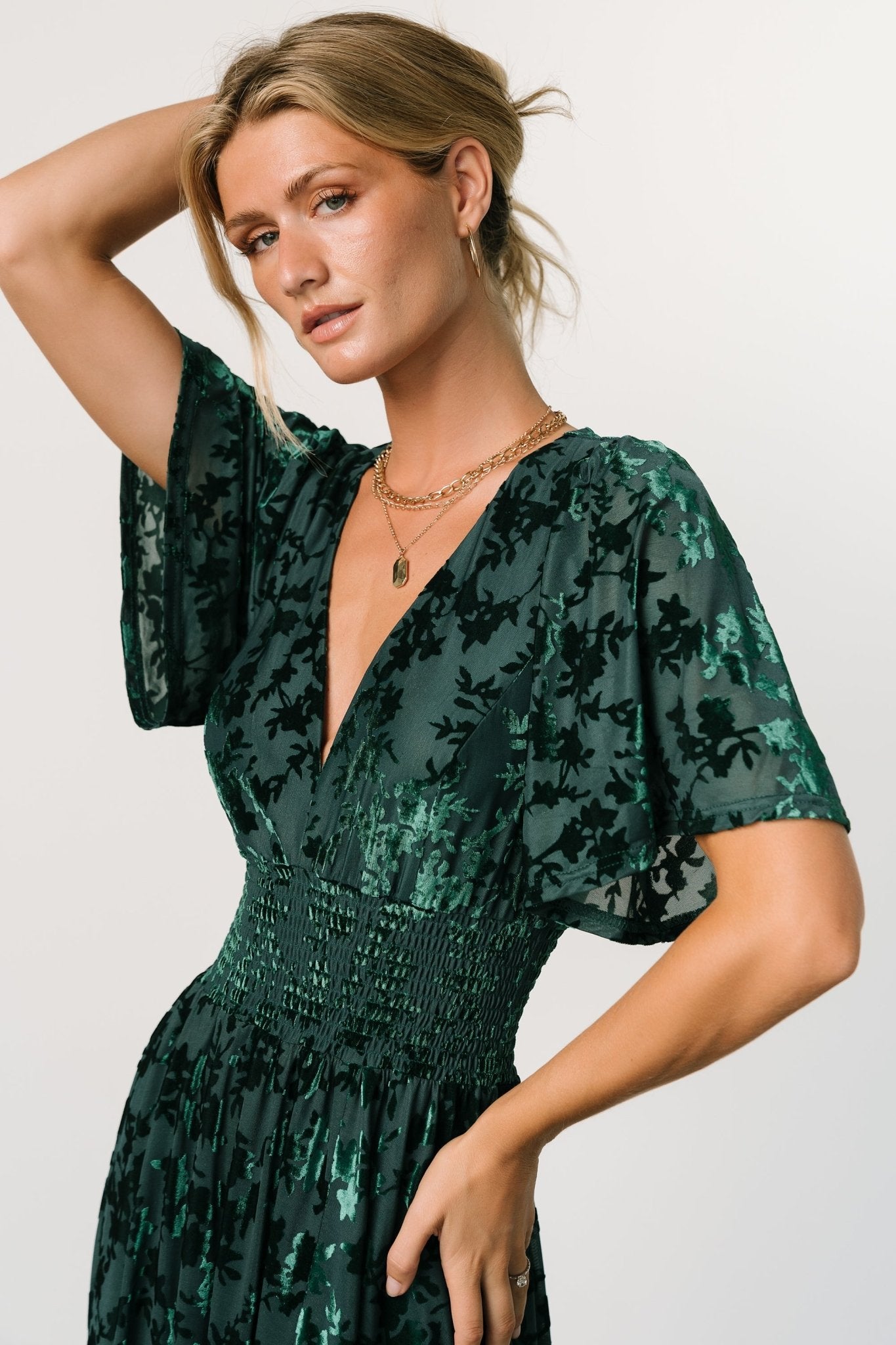 Full-length shot of green embossed velvet maxi dress displaying deep V-neck, flowy sleeves, smocked waist and left leg slit.