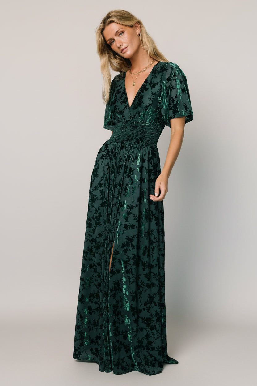 Front view of green embossed velvet maxi dress with deep V-neck, smocked waist, flowy short sleeves, and left-side leg slit for movement.