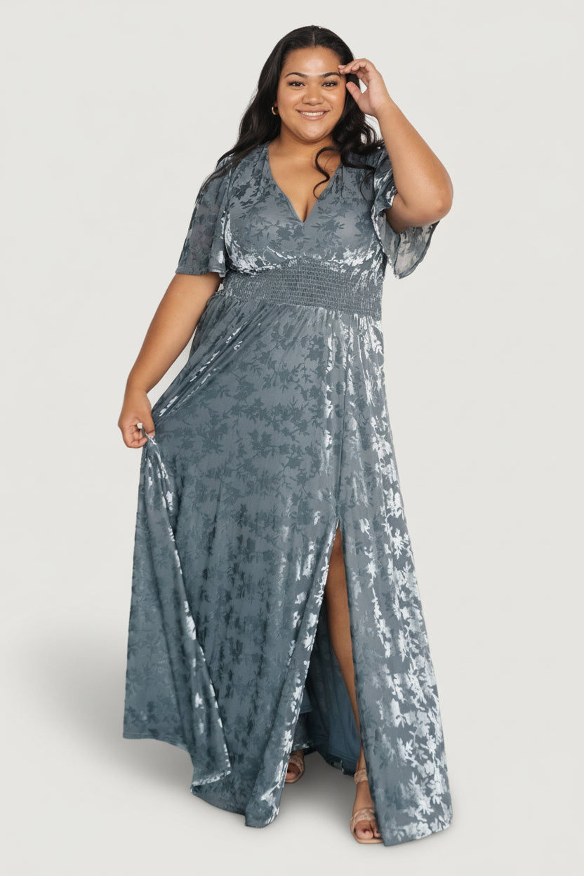 Three-quarter view of Veronica velvet maxi in slate blue highlighting smocked waist, gentle drape of fabric, and movement at the skirt with embroidered texture.