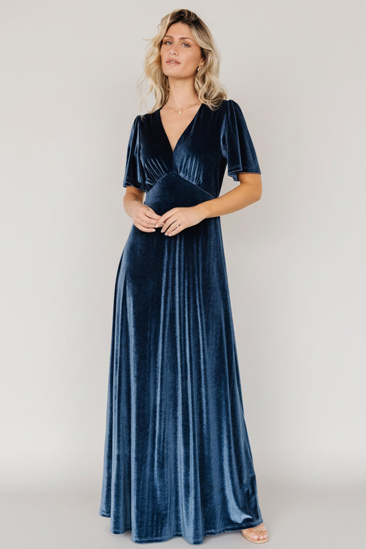 Front view of blue Vivian velvet maxi dress on model showing deep V-neckline, flutter sleeves, gathered bust, and flowing skirt, highlighting drape and sheen.
