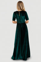 Styled shot of the emerald Vivian velvet maxi dress paired with heels, showing full silhouette, deep V-neck, and gown-length hem.