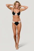 Front view of Vixen bikini bottom in black and sand on model, classic hip cut with moderate coverage and visible lining.