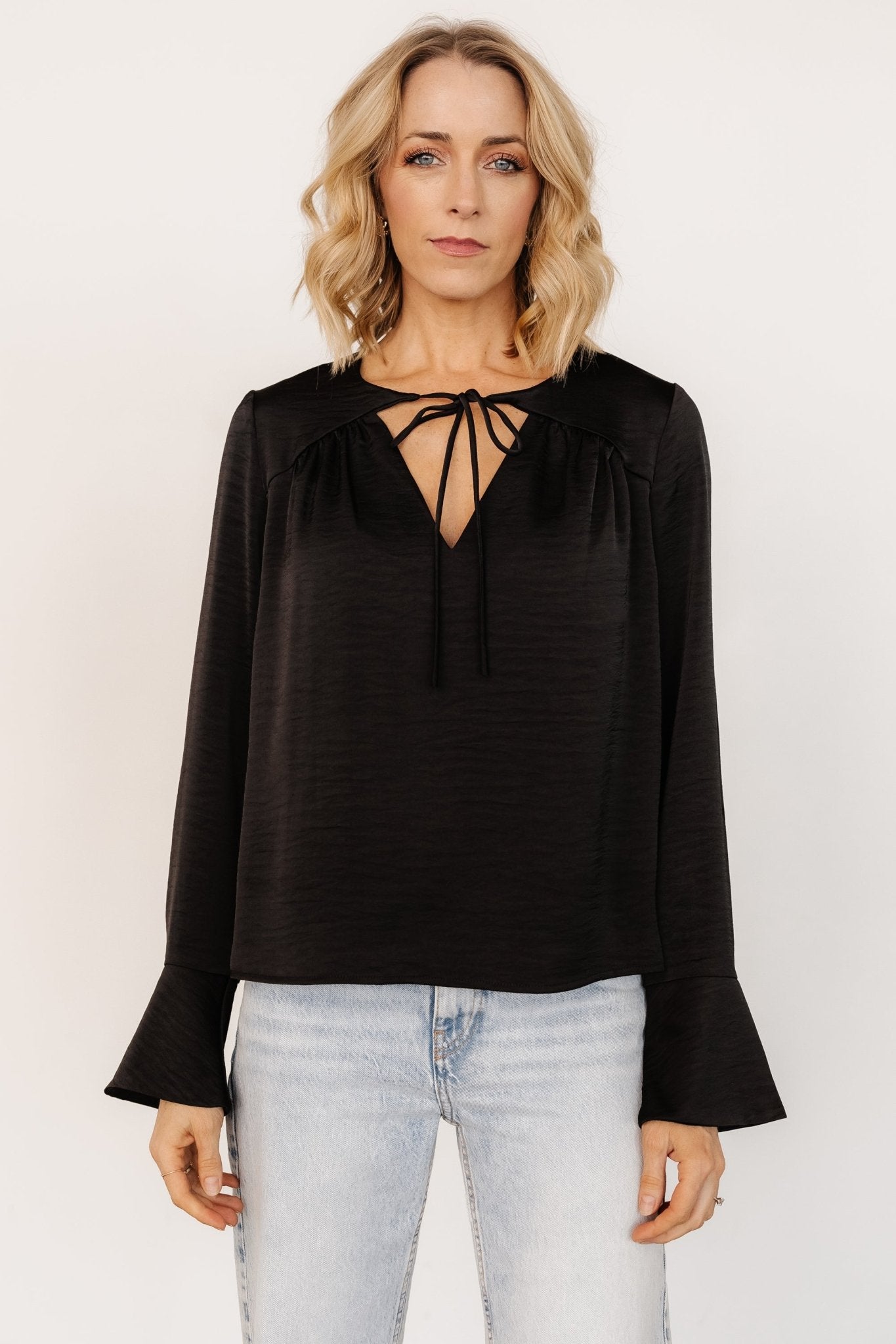 Front view of Westminster Satin Top in black showing textured satin-like fabric, V-neck tie, pleated bust and long bell cuffs.