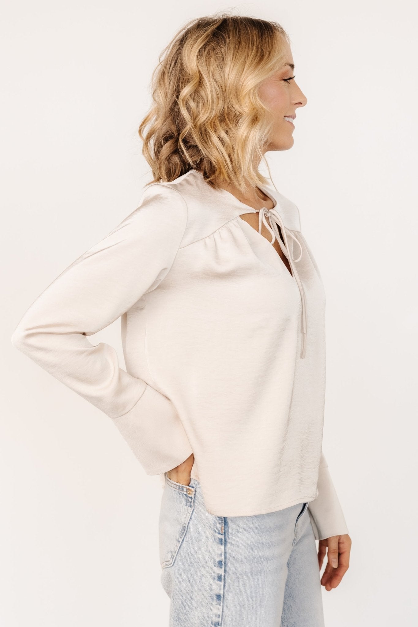 Side view of blouse tucked into pants, showing drape, unlined construction and bell sleeve silhouette in pearl champagne.