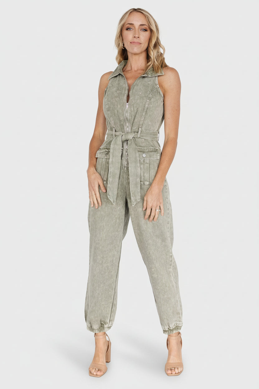 Front view of washed olive sleeveless denim jumpsuit on model, showing notch collar, belt and jogger-style ankles.