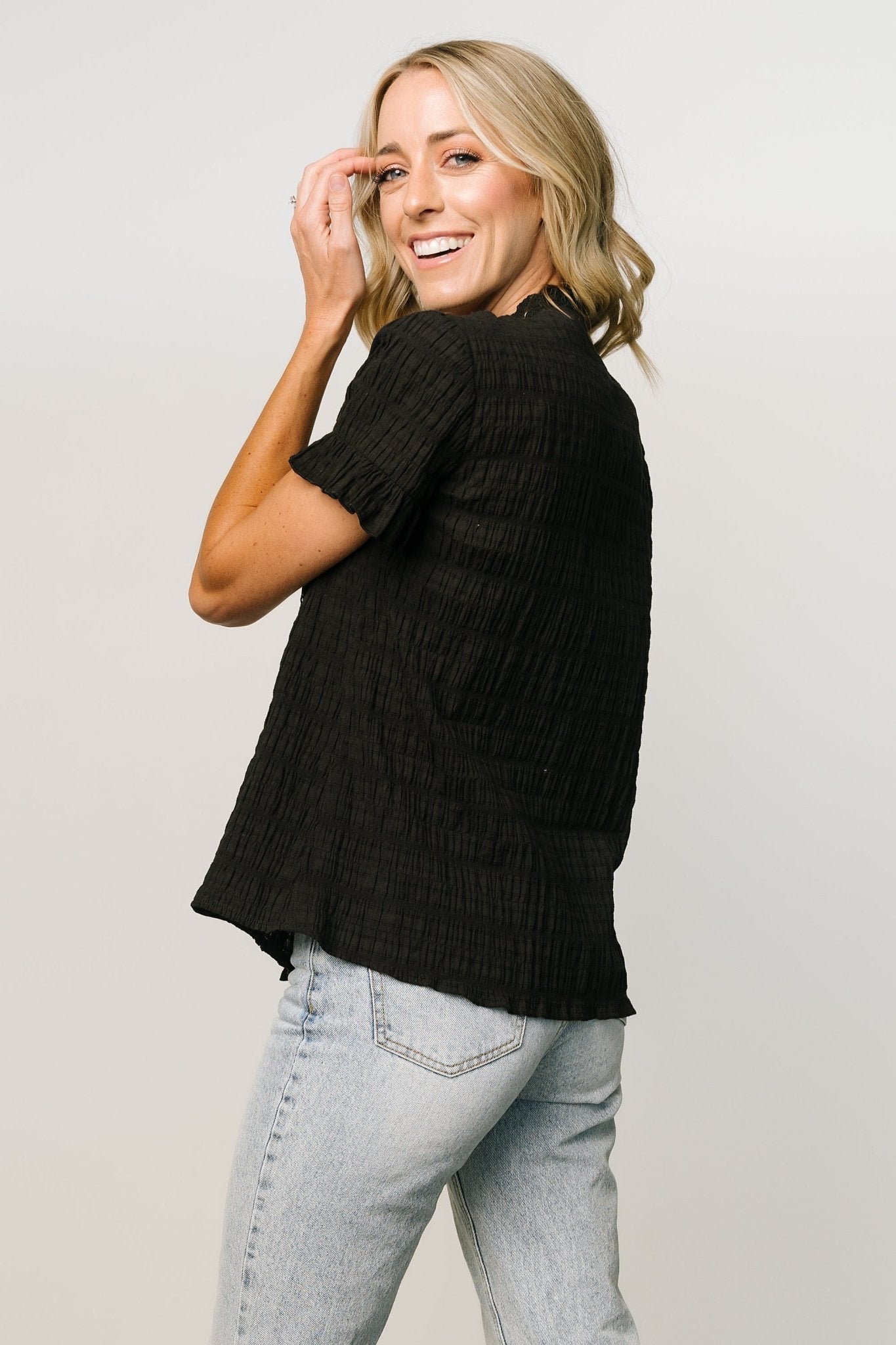 Side view of black Zara lace top showing short ruffle sleeve profile, lightweight unlined bodice, and gentle drape over the shoulder and arm