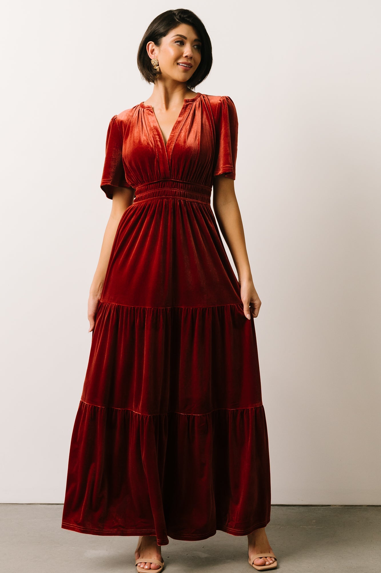 Three-quarter side view of Artemis terracotta velvet maxi dress showing flutter sleeve detail and the soft drape of the tiered skirt.