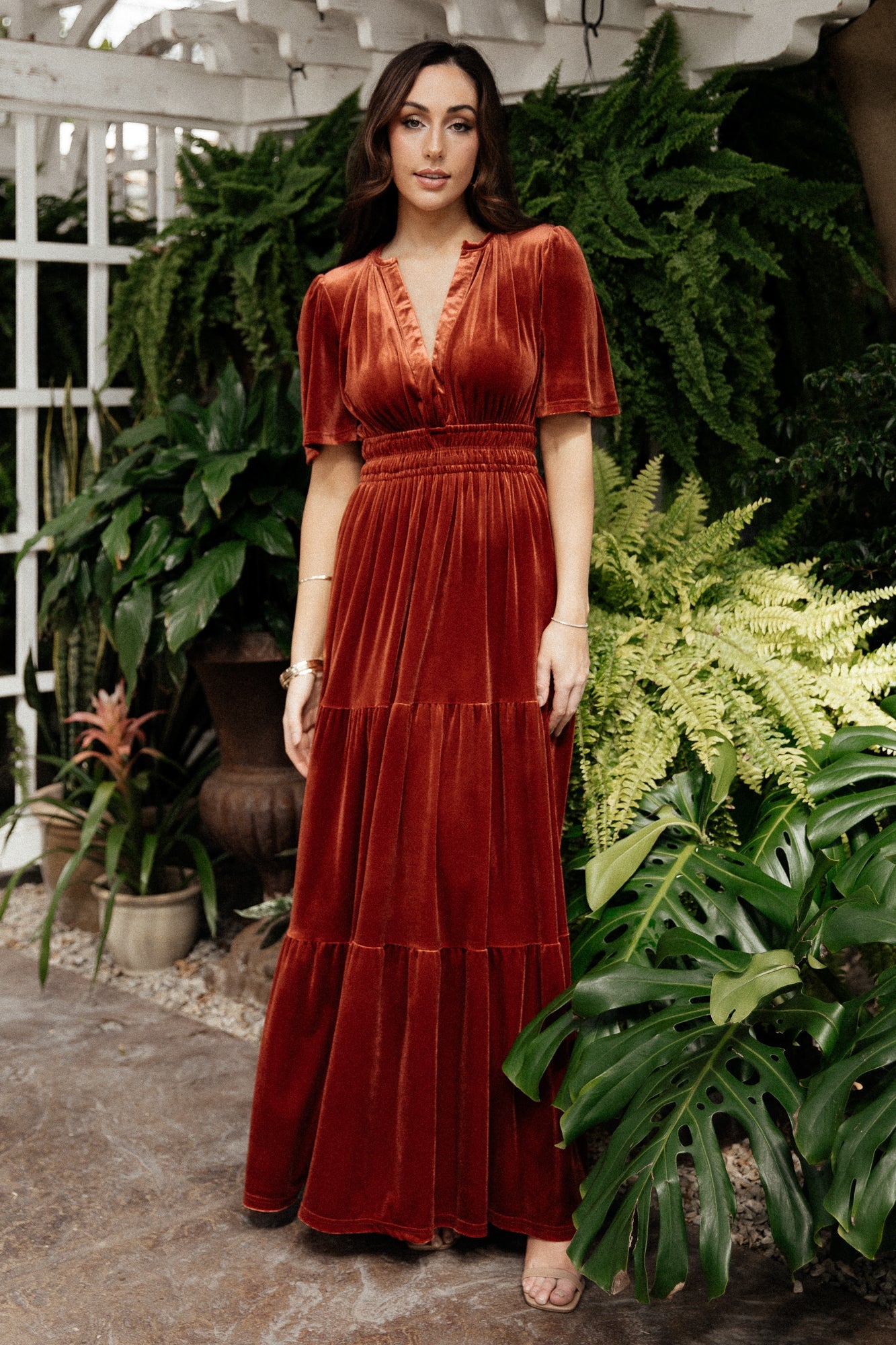 Front model view of Artemis terracotta velvet maxi dress with plunging V-neck, short flutter sleeves, elastic waist, and tiered flowing skirt.