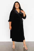 Side-angle shot of velvet wrap midi showing drape of skirt, wrap overlap and subtle velvet texture on a black evening silhouette.