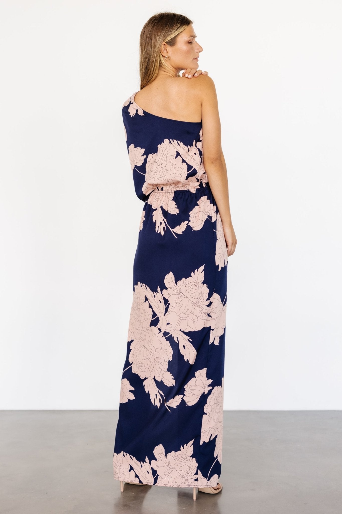 Full-length shot of the Halston one-shoulder maxi in navy and blush, highlighting the flowing skirt, left-side cutout, and evening-ready silhouette.