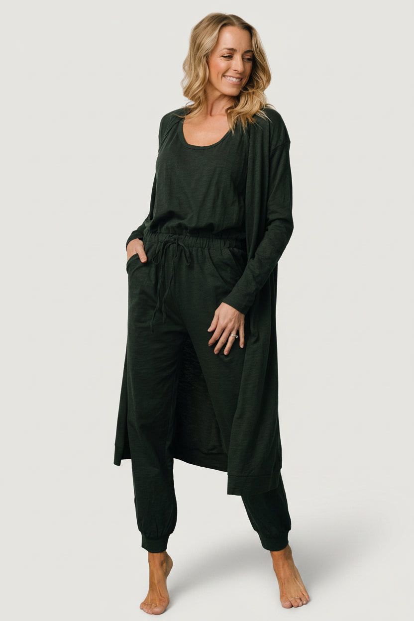Front view of dark green 100% cotton tank jumpsuit with adjustable tie waist and matching oversized long-sleeve cardigan on model, showing full outfit.