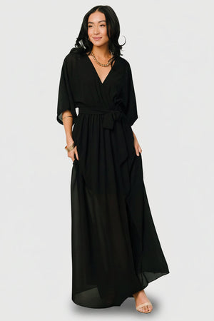 Front view of Kia Kimono Maxi Dress in black showing crossover surplice neckline, elastic waist and flowing maxi skirt with left slit (model view).