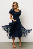 Styled look of the navy Liv tulle midi dress paired with neutral shoes, illustrating length, movement, and occasion-ready styling.