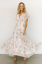 Model wearing off-white printed chiffon Lynlee maxi with subtle metallic thread, flowing A-line skirt and smocked waist; three-quarter front pose.