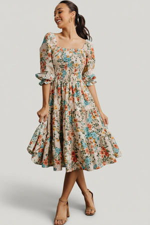 Front view of smocked midi dress in bright multi floral print, square neckline, smocked bodice and tiered flowing skirt, model pose