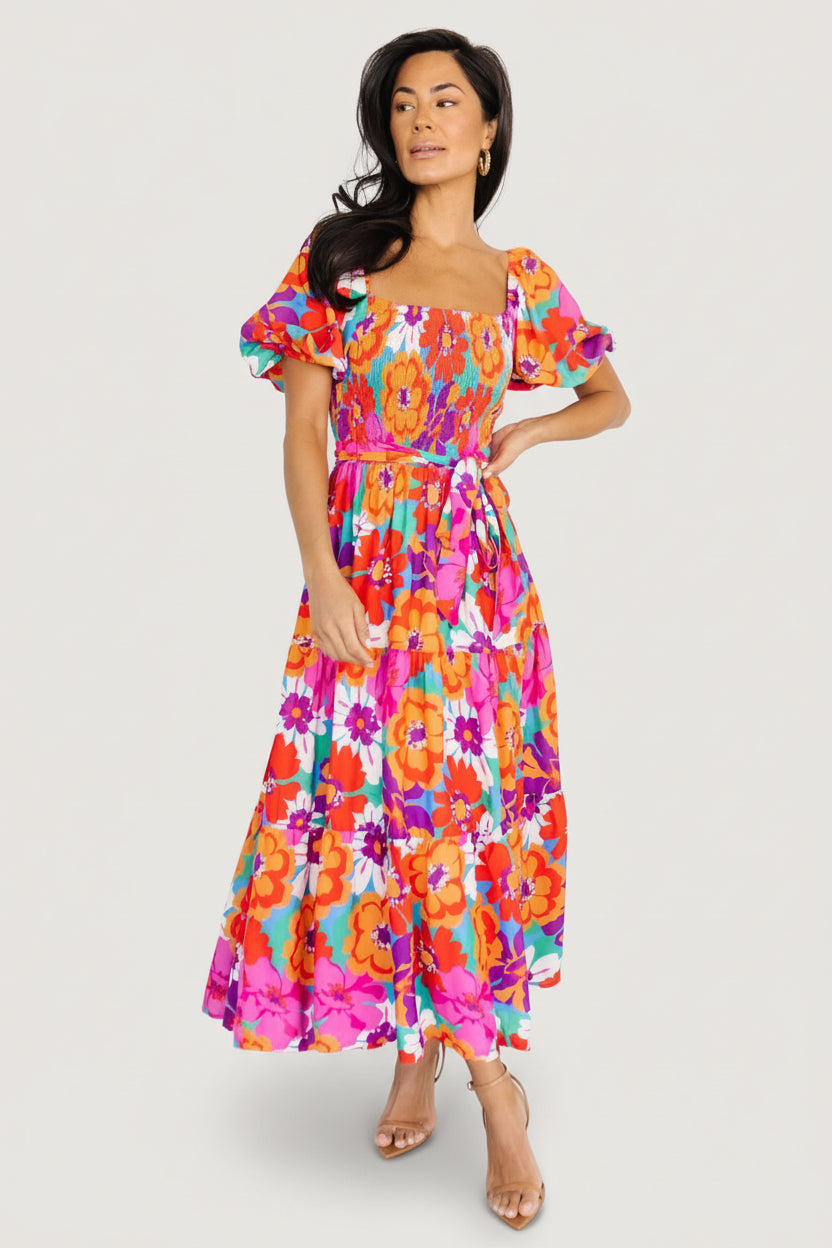 Front view of smocked square-neck maxi dress in multi-colored floral print, short gathered sleeves and ruffled hem creating soft movement.