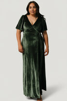 Side profile of the Meghan velvet wrap maxi in deep green, showing sleeve shape, side drape, and tulip hem movement on the model.