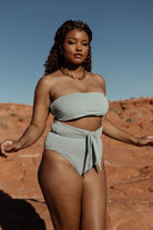 Model wearing Milos sage bandeau bikini top, close-up of neckline and soft stretch fabric highlighting subtle sage color and fit.