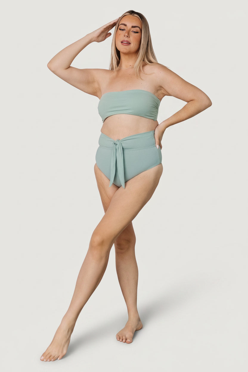 Lifestyle shot of model in Milos sage bandeau top at the beach, highlighting color, fit, and easy styling for vacation wear.