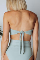 Studio shot of Milos sage bandeau bikini top flat-lay showing color accuracy, fabric sheen, and tie-back feature laid out.