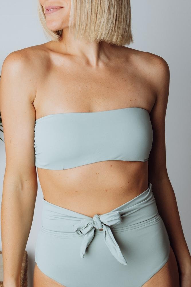 Three-quarter view of Milos sage bikini top on model, showing silhouette, adjustable tie-back, and how the top pairs with high-waist bottoms.