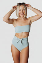 Front view of Milos sage bandeau bikini top on model showing tie-back detail, removable pads, and smooth nylon-spandex fabric in sage tone.