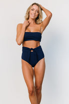 Model wearing navy Milos high-waist bikini bottom with front tie detail, showing moderate coverage and how the waistband sits at the natural waist.