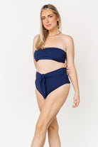 Close-up of front tie detail on navy high-waist bikini bottom, emphasizing adjustable wrap, knot styling, and fabric hand.